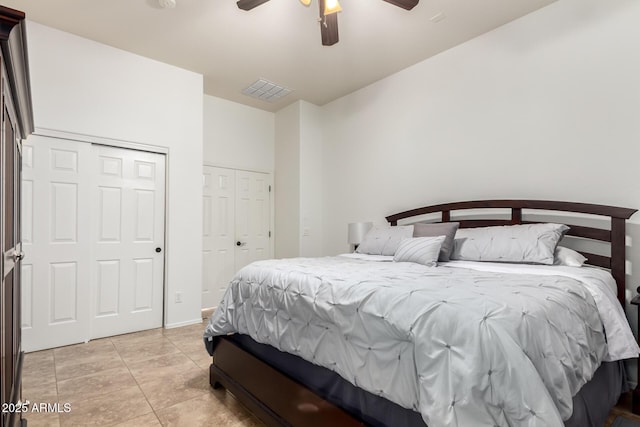 bedroom with light tile patterned flooring, visible vents, two closets, and a ceiling fan