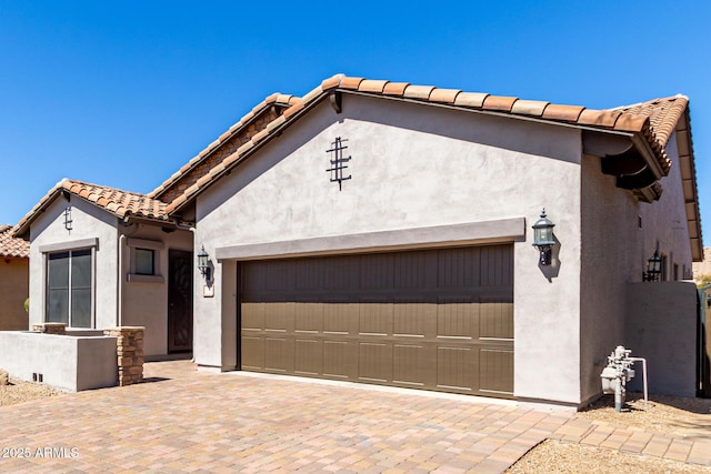 view of front facade featuring decorative driveway, stucco siding, a tiled roof, and a garage
