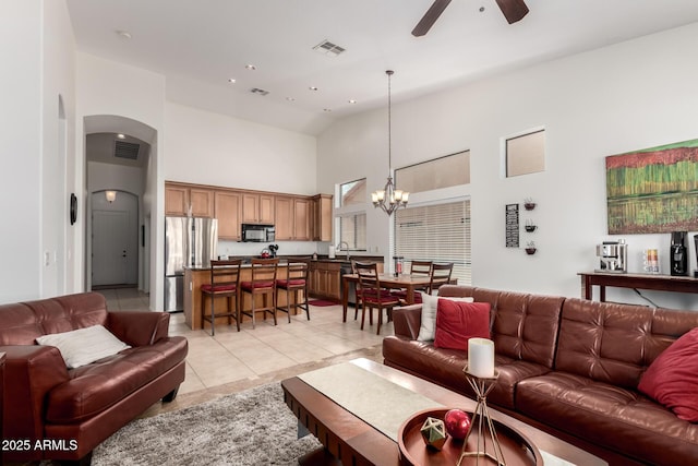 living area with light tile patterned floors, high vaulted ceiling, ceiling fan with notable chandelier, arched walkways, and visible vents
