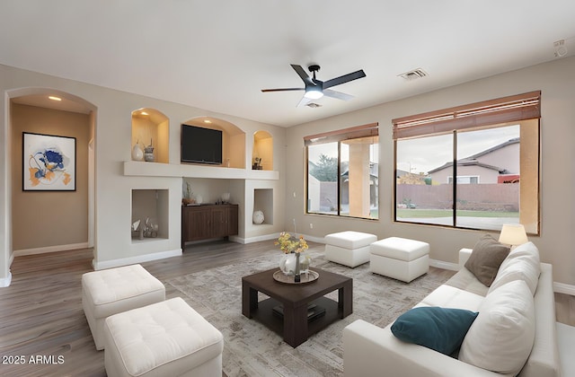 living room featuring built in shelves, ceiling fan, and light wood-type flooring