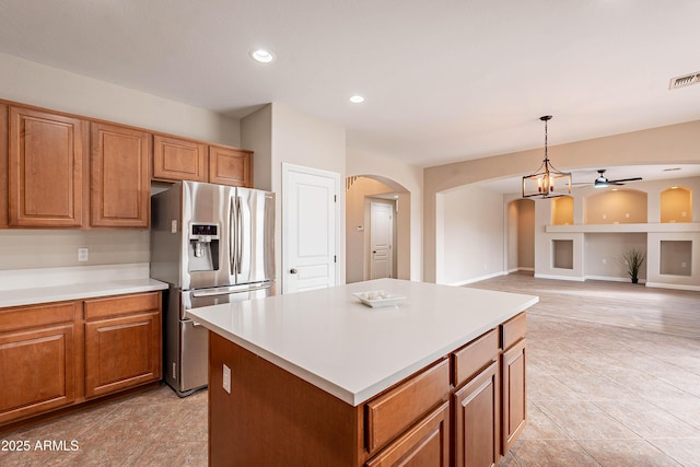 kitchen with built in shelves, hanging light fixtures, stainless steel fridge, a kitchen island, and ceiling fan with notable chandelier