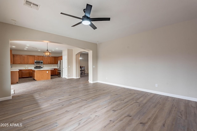 unfurnished living room with ceiling fan with notable chandelier and light wood-type flooring