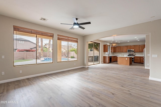 unfurnished living room featuring ceiling fan with notable chandelier, light hardwood / wood-style floors, and sink