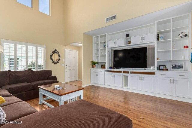 living area with a towering ceiling, arched walkways, visible vents, and light wood finished floors