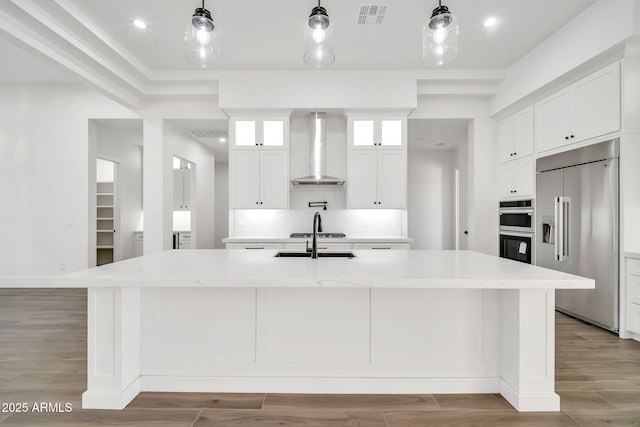 18225 W San Juan Ct, Litchfield Park, AZ 85340 - kitchen featuring appliances with stainless steel finishes, wall chimney exhaust hood, a large island with sink, a sink, and white cabinetry