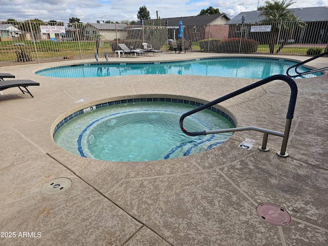 pool with a patio area, a community hot tub, and fence