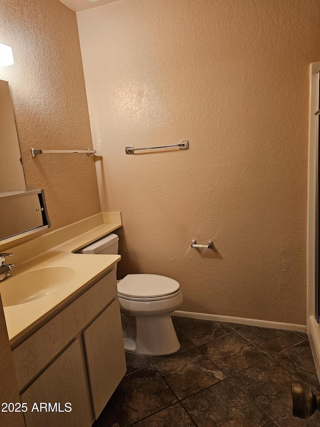 bathroom featuring baseboards, toilet, vanity, and a textured wall