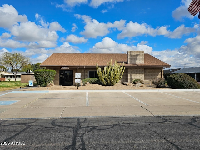 view of front facade with brick siding, uncovered parking, and a shingled roof