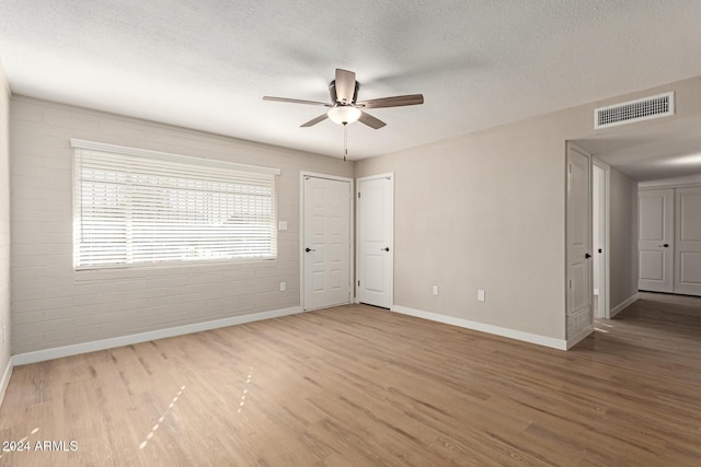 spare room featuring ceiling fan, wood-type flooring, a textured ceiling, and brick wall