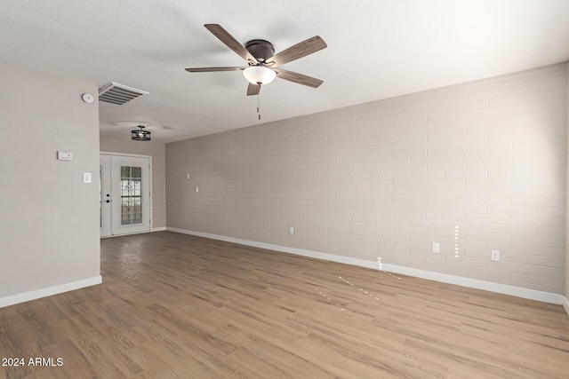 empty room featuring ceiling fan, a textured ceiling, brick wall, and light hardwood / wood-style flooring