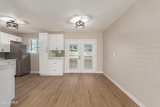 kitchen featuring french doors, brick wall, light hardwood / wood-style flooring, white cabinetry, and stainless steel refrigerator