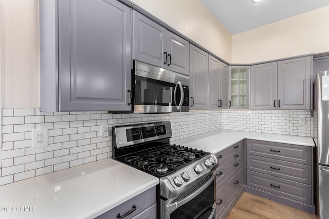 kitchen featuring stainless steel appliances, tasteful backsplash, gray cabinetry, and light hardwood / wood-style flooring