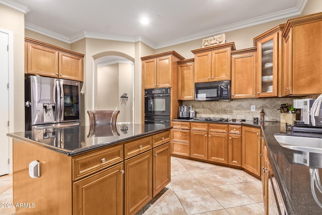 kitchen featuring a kitchen island, ornamental molding, dark stone countertops, black appliances, and sink