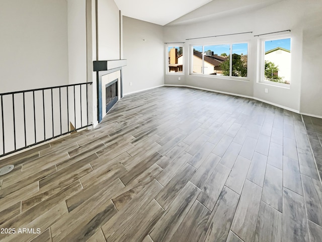 unfurnished living room with baseboards, vaulted ceiling, wood finished floors, and a tile fireplace