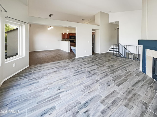 unfurnished living room featuring baseboards, a high ceiling, visible vents, a fireplace, and wood finished floors