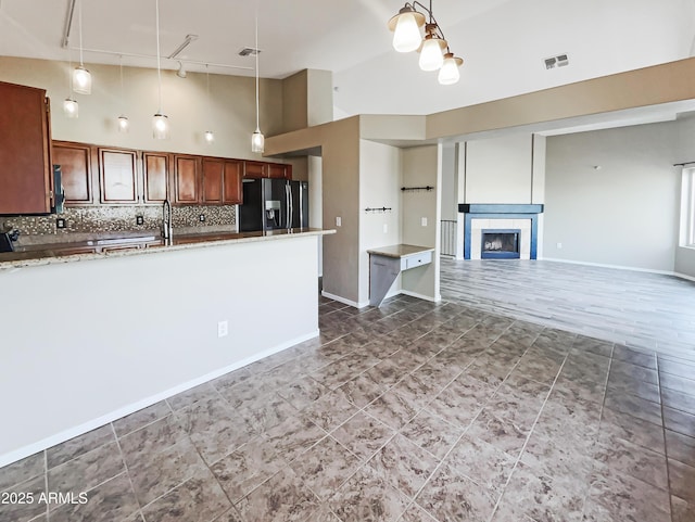 kitchen featuring decorative backsplash, visible vents, black fridge, hanging light fixtures, and a high ceiling