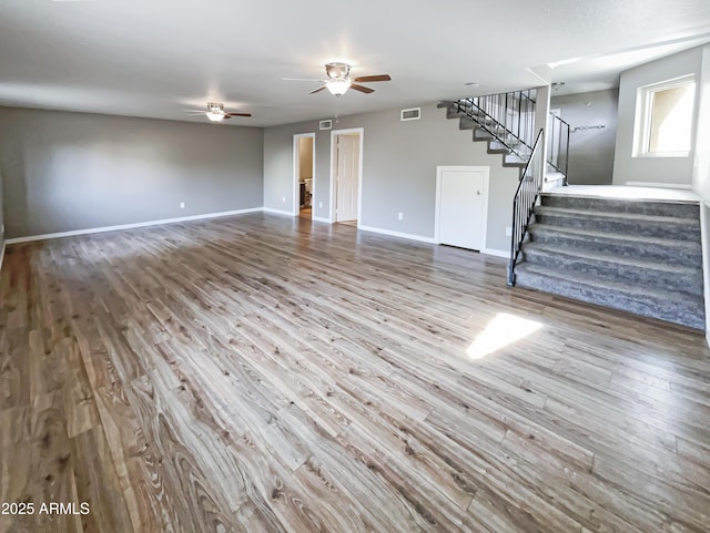 unfurnished living room featuring stairway, a ceiling fan, wood finished floors, baseboards, and visible vents