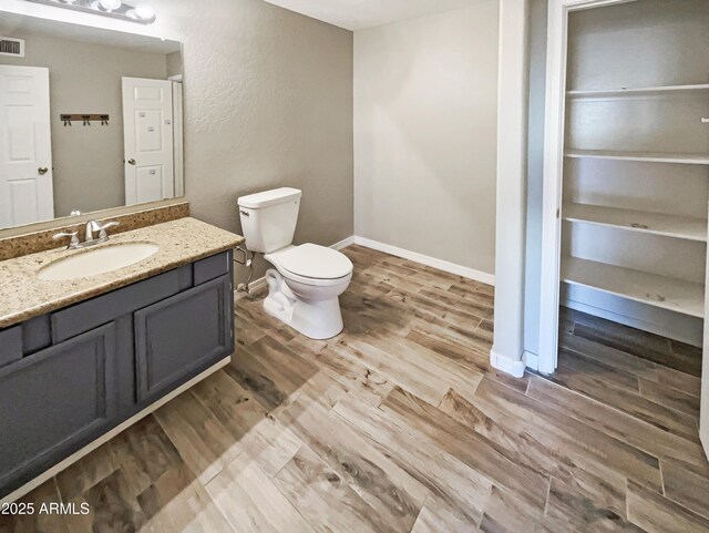 bathroom featuring vanity, toilet, baseboards, visible vents, and wood finished floors