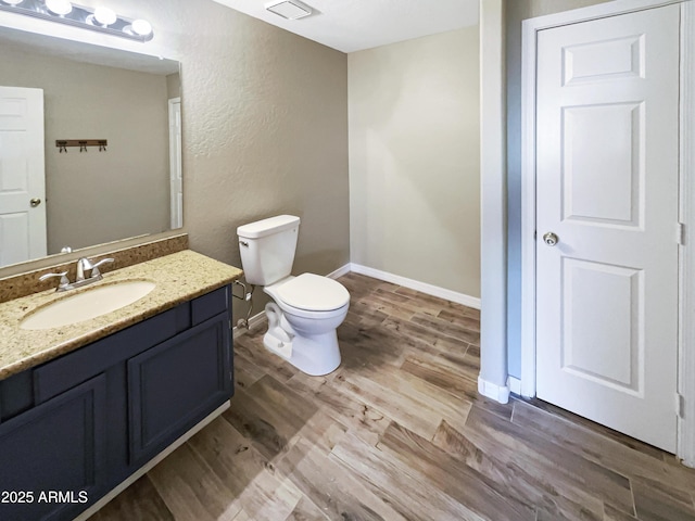 bathroom with toilet, vanity, baseboards, and wood finished floors