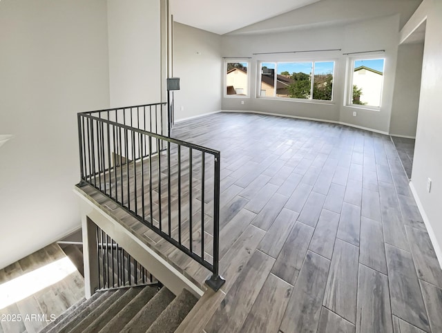 spare room featuring baseboards, high vaulted ceiling, and wood finished floors