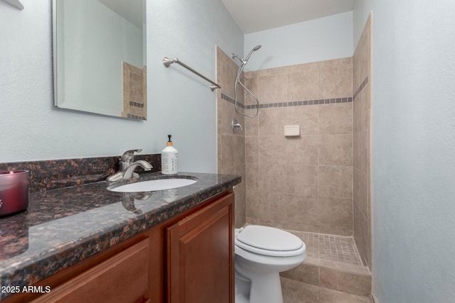 bathroom featuring tile patterned floors, vanity, toilet, and a tile shower