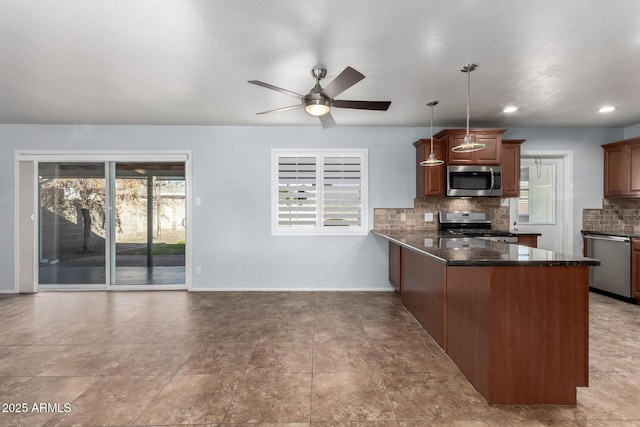 kitchen with hanging light fixtures, decorative backsplash, dark stone countertops, appliances with stainless steel finishes, and kitchen peninsula