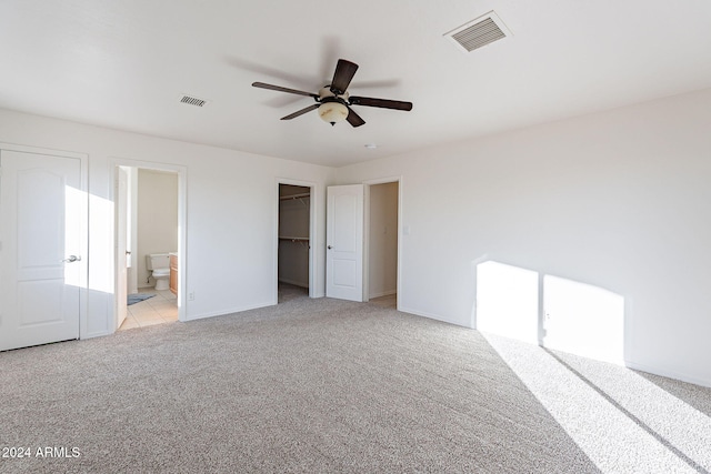 unfurnished bedroom featuring ensuite bath, ceiling fan, light colored carpet, a walk in closet, and a closet