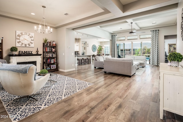 living room with coffered ceiling, ceiling fan with notable chandelier, light wood-type flooring, and beam ceiling