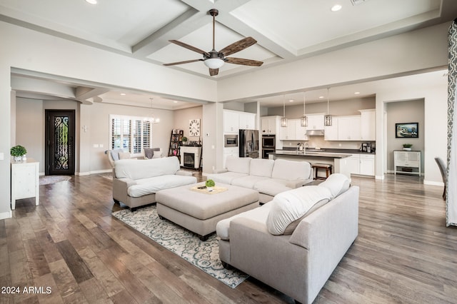 living room featuring ceiling fan with notable chandelier, beamed ceiling, hardwood / wood-style flooring, and coffered ceiling