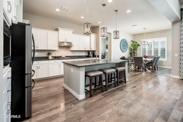 kitchen featuring white cabinets, an island with sink, pendant lighting, appliances with stainless steel finishes, and light wood-type flooring