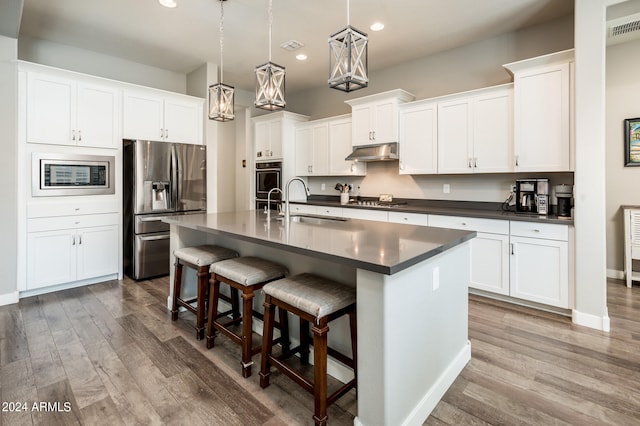 kitchen with white cabinetry, a kitchen island with sink, stainless steel appliances, and decorative light fixtures