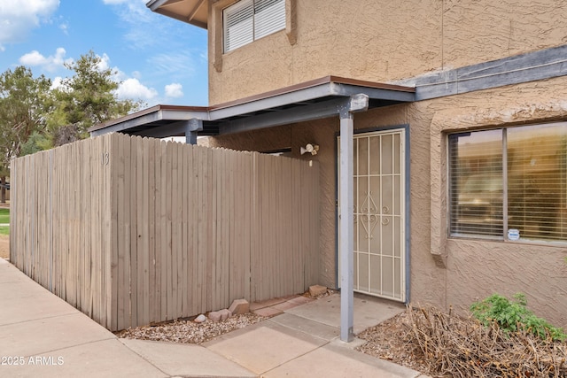 doorway to property featuring stucco siding and fence