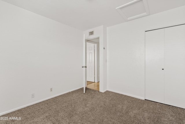 unfurnished bedroom with attic access, carpet floors, a closet, and baseboards