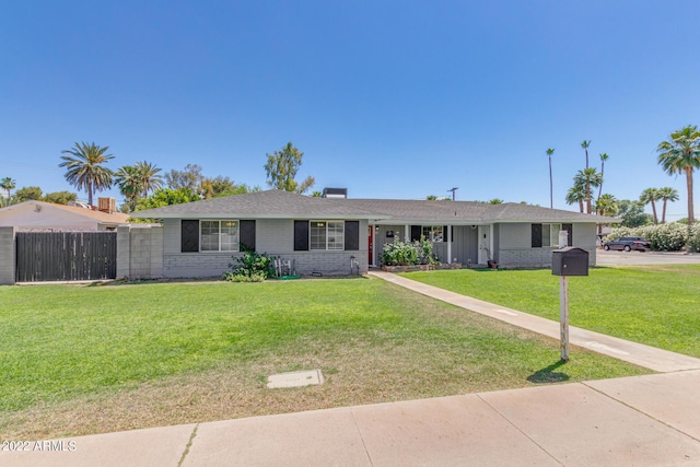 ranch-style home featuring brick siding, a front lawn, and fence