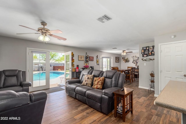 living room with dark wood-style floors, visible vents, ceiling fan, and baseboards