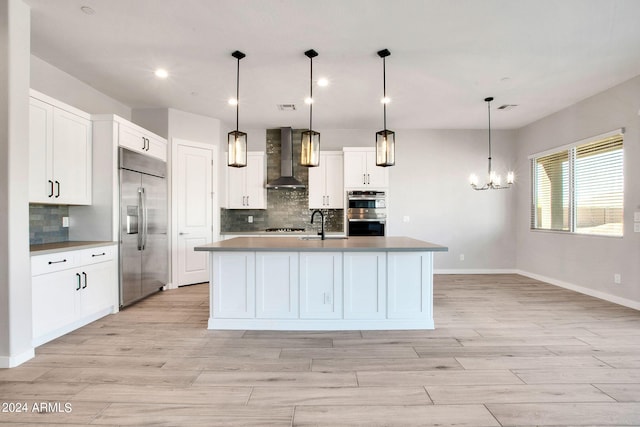 kitchen featuring stainless steel appliances, wall chimney range hood, light wood-type flooring, and a notable chandelier