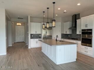 kitchen featuring white cabinets, a center island with sink, wall chimney exhaust hood, and stainless steel appliances