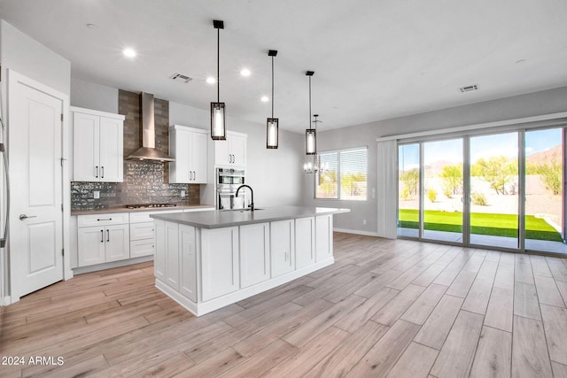 kitchen featuring visible vents, wall chimney range hood, appliances with stainless steel finishes, decorative backsplash, and light wood finished floors