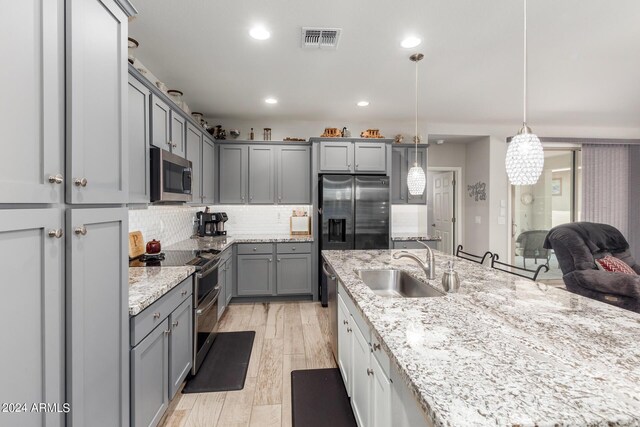 kitchen featuring a breakfast bar area, appliances with stainless steel finishes, gray cabinetry, light stone countertops, and an island with sink