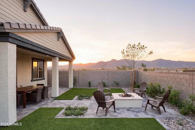 patio terrace at dusk with a mountain view, a yard, and an outdoor fire pit