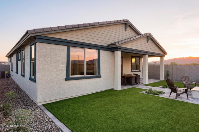 back house at dusk with a lawn, a patio, and central AC unit