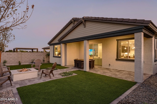 back house at dusk featuring a lawn, a patio area, and a fire pit