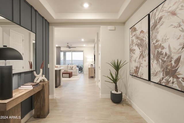 hall with a tray ceiling and light wood-type flooring