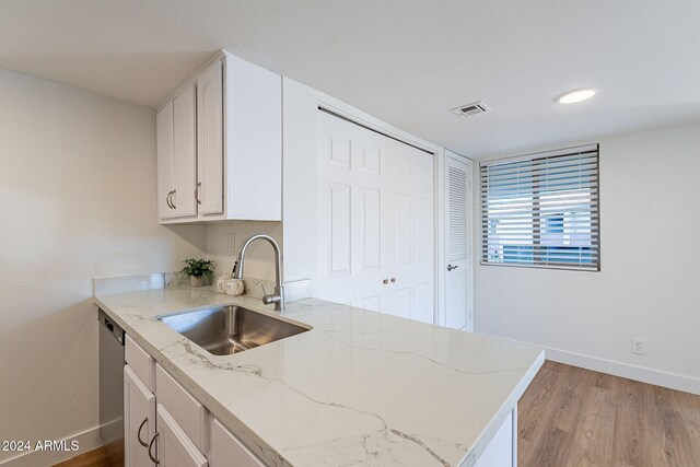 kitchen with light stone countertops, kitchen peninsula, light wood-type flooring, sink, and white cabinetry