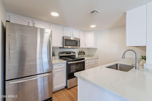 kitchen with white cabinetry, sink, stainless steel appliances, light stone counters, and light wood-type flooring