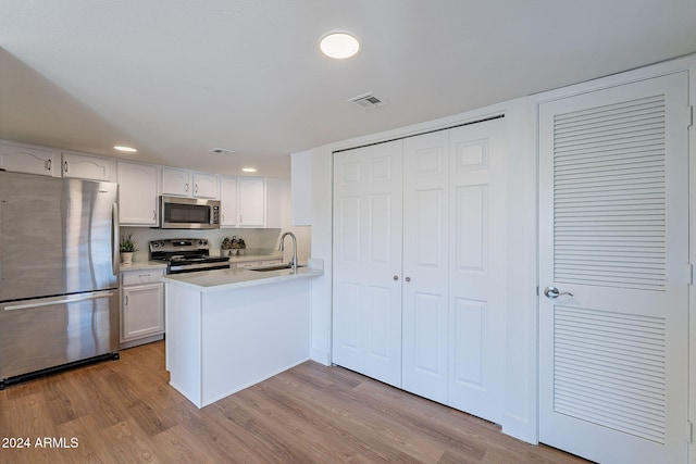 kitchen featuring white cabinetry, sink, stainless steel appliances, kitchen peninsula, and light hardwood / wood-style floors