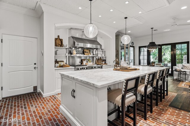 kitchen featuring pendant lighting, white cabinetry, wall chimney exhaust hood, and an island with sink