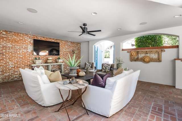 living room with a brick fireplace, ceiling fan, and brick wall