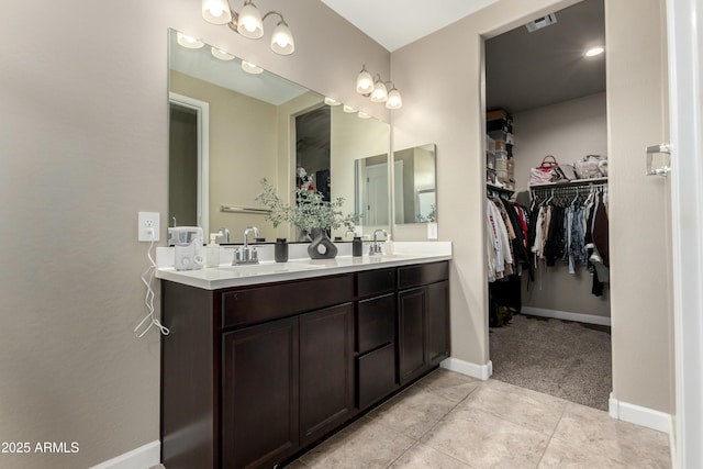 bathroom featuring visible vents, a walk in closet, a sink, double vanity, and baseboards