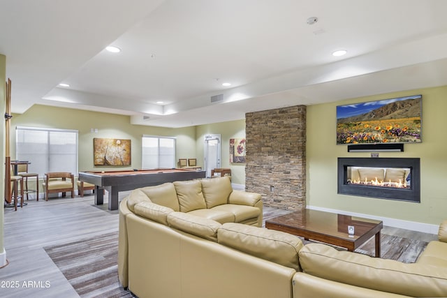 living room featuring pool table, a fireplace, light wood-type flooring, and a raised ceiling